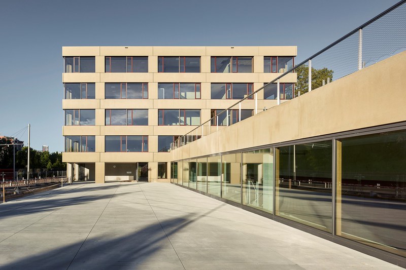 Die Aussenaufnahme zeigt das moderne Schulhaus Brünnen kurz nach seiner Fertigstellung 2016. Die klar gegliederte Fassade wird dominiert von grossen Fenstern und gelbgoldenen Fassadenelementen.